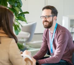 A shopware employee is sitting across from a woman and smiles during a conversation.