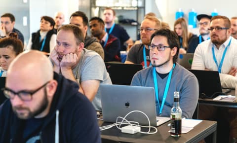 A group of Hackathon participants are attentively listening to a presentation.