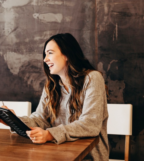 A woman is smiling and looking to the side, holding a tablet.