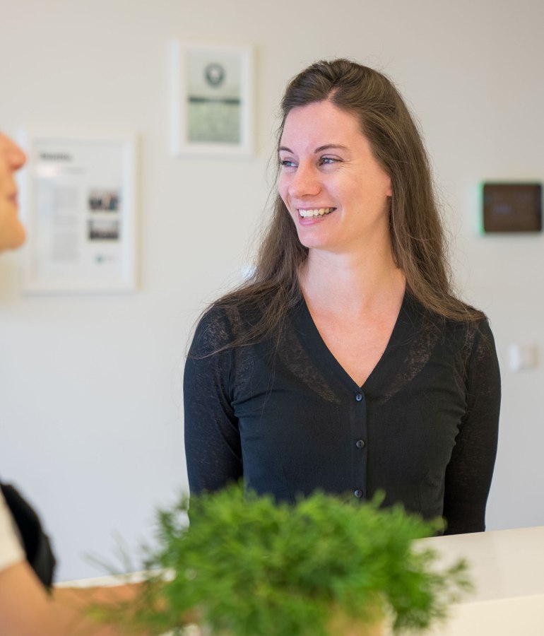 Woman is smiling and standing in an office area.